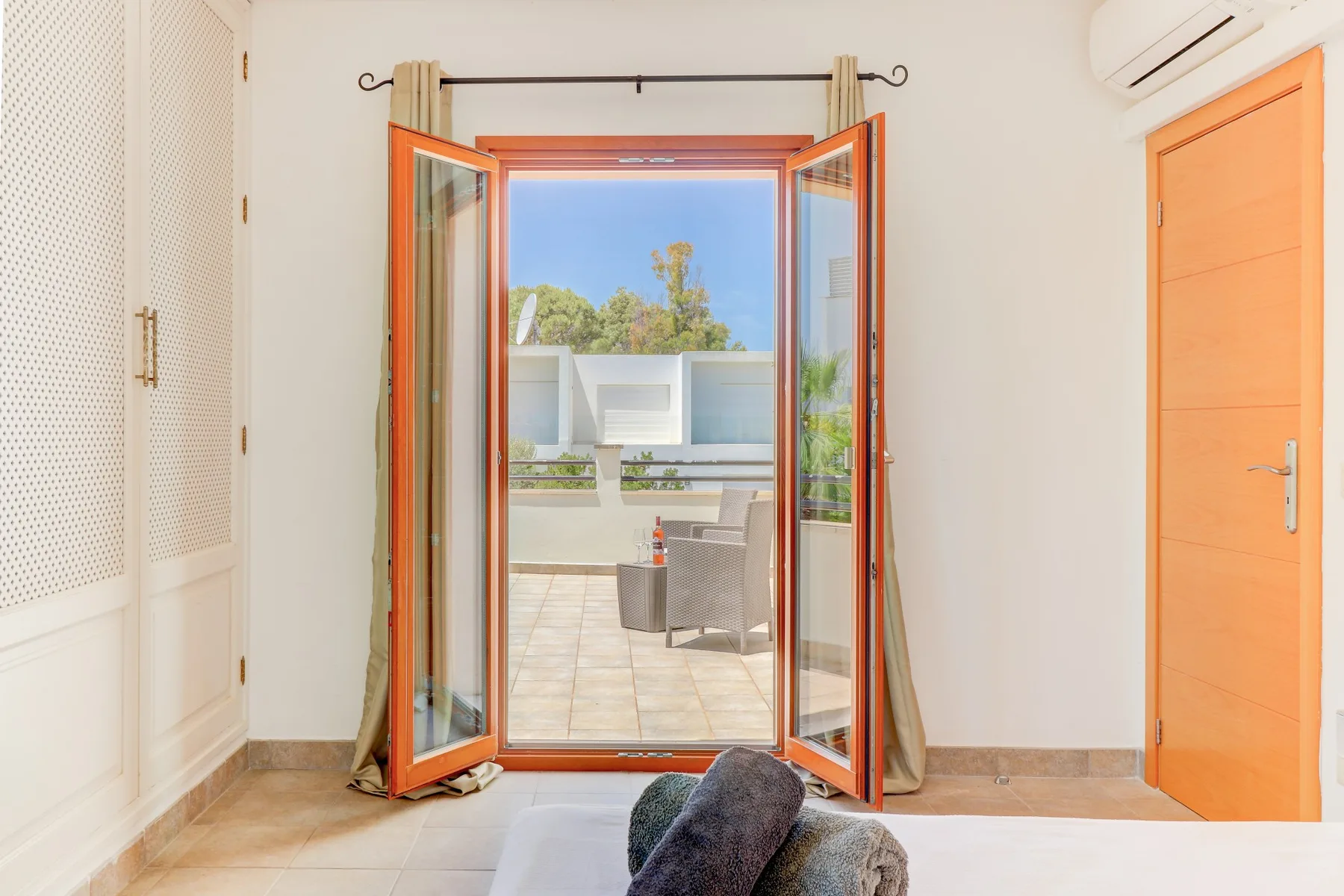 A bright room opens through orange-framed doors onto a tiled terrace.