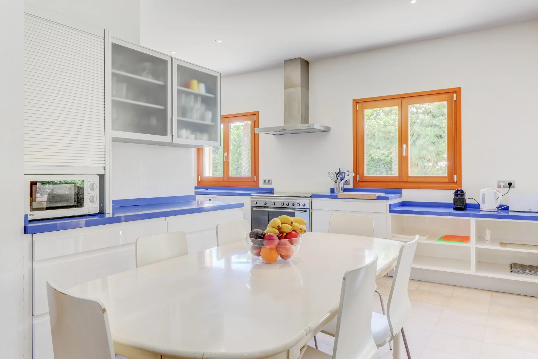 A bright kitchen with white cabinetry, blue countertops, and a dining table.
