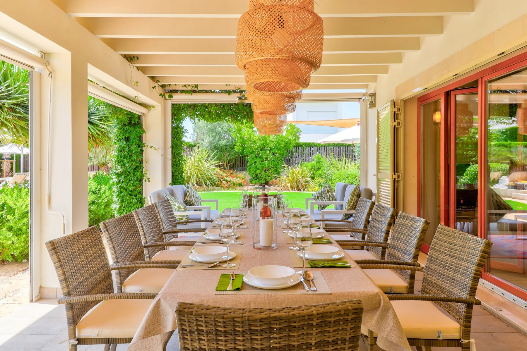 A covered patio dining area with a long table and woven seating.