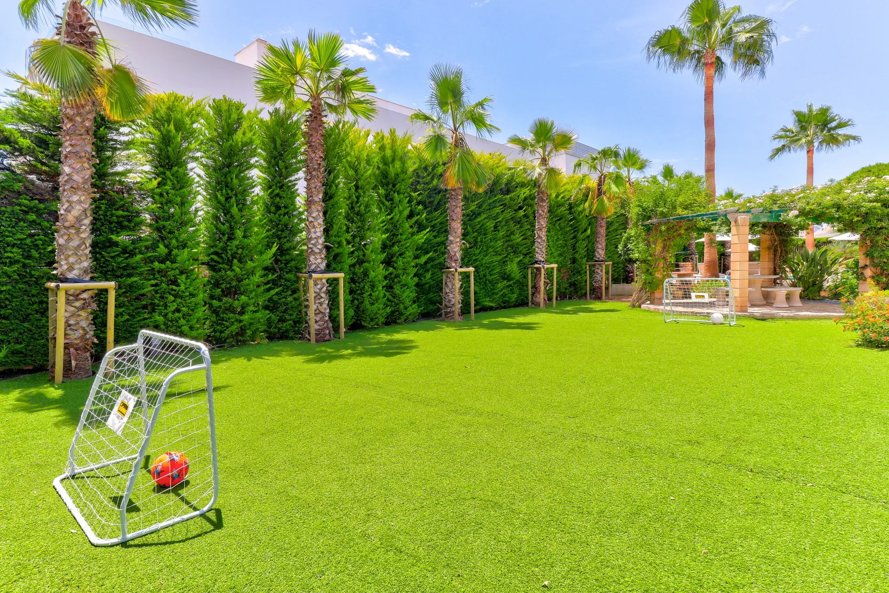 A green lawn with a small soccer goal, palm trees, and a shaded seating area.