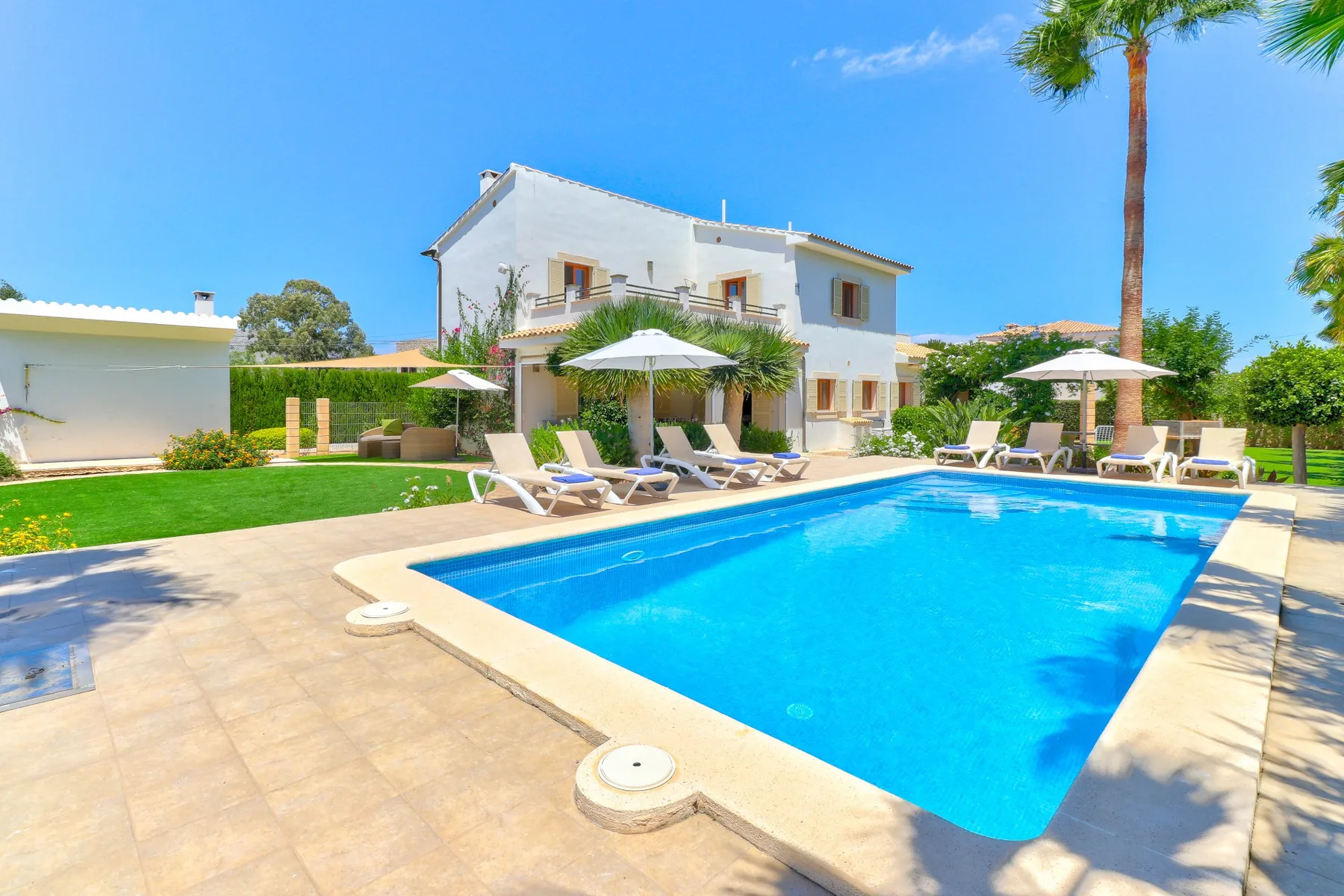 A swimming pool sits beside a white house, with loungers arranged around the patio.