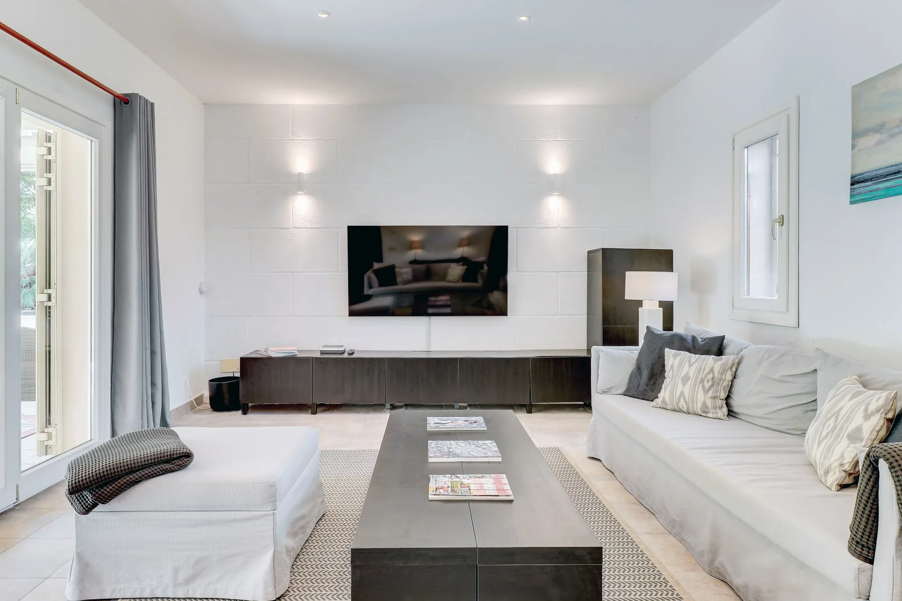 A bright living room with a wall-mounted television and seating around a coffee table.