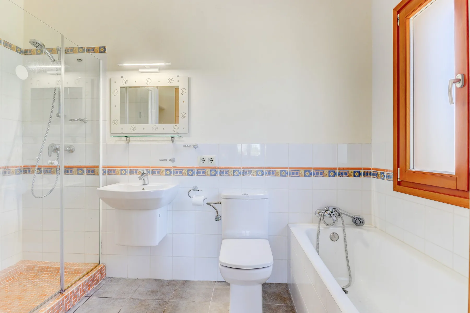 A bright bathroom with a glass shower, sink, toilet, and bathtub.