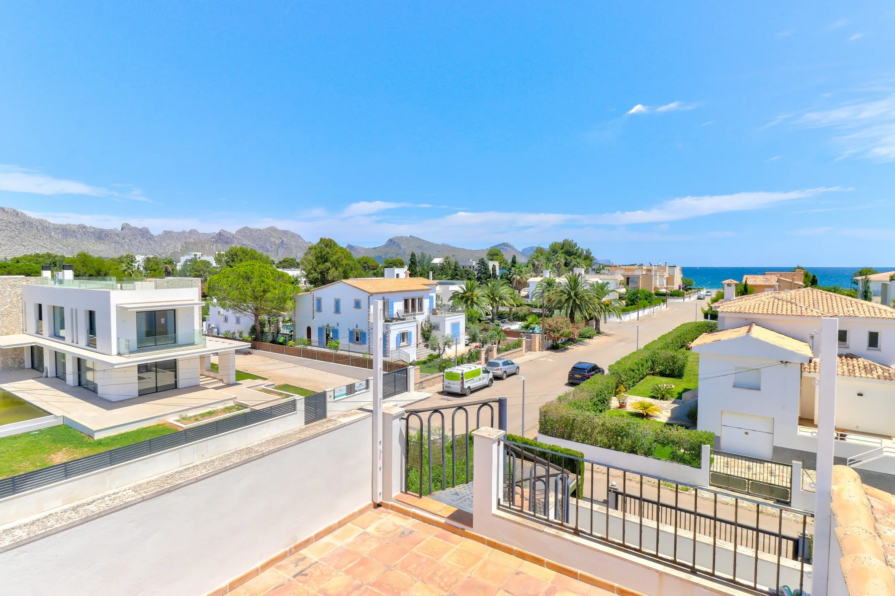A coastal residential neighborhood with houses, greenery, and the sea in the distance.