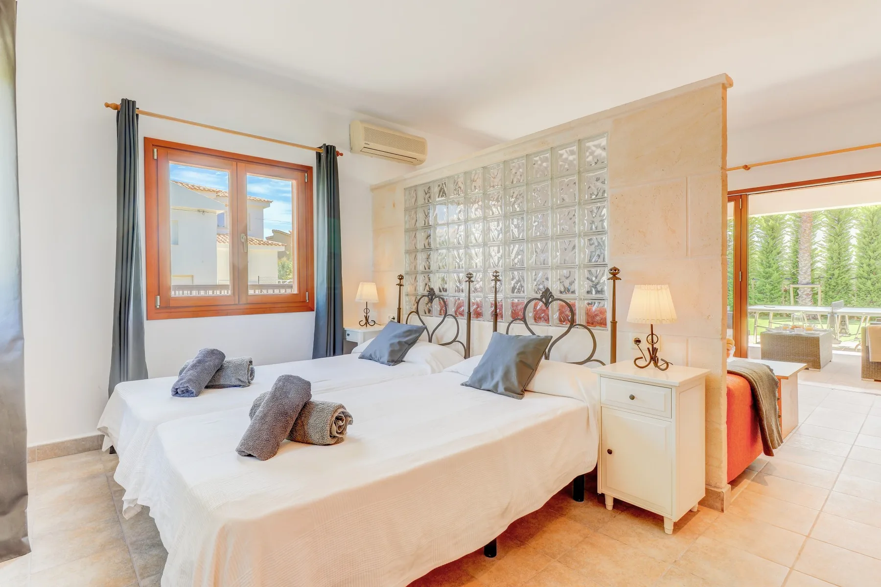 A bright bedroom with two beds and a glass-block divider.