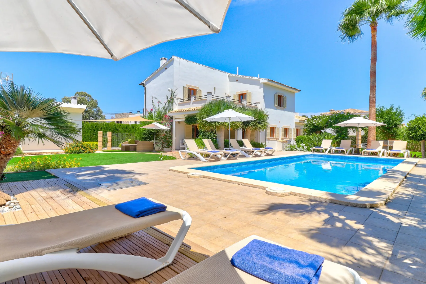An outdoor swimming pool beside a white house, with loungers on the surrounding patio.
