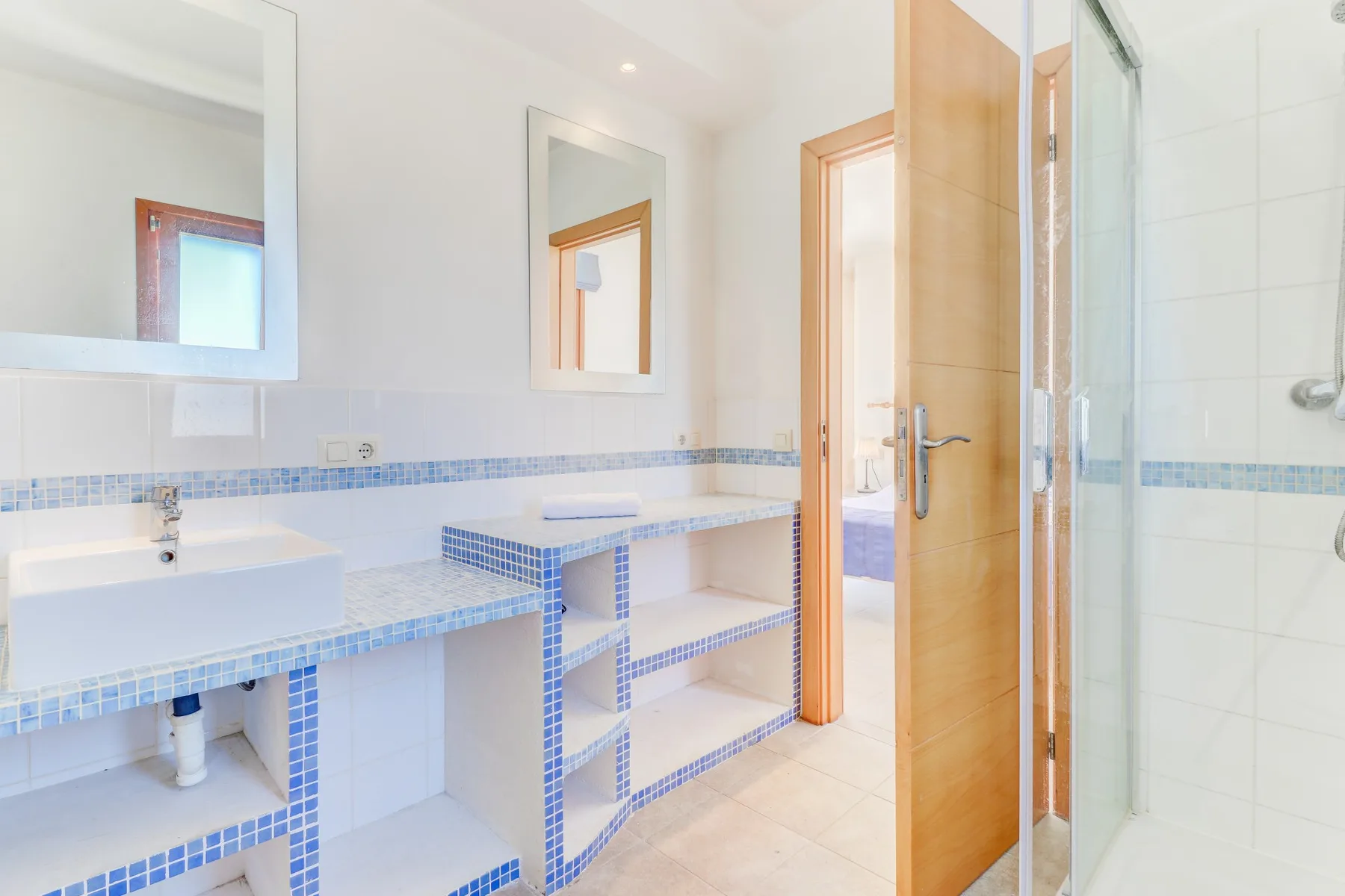A bright tiled bathroom with a long vanity and a glass shower.