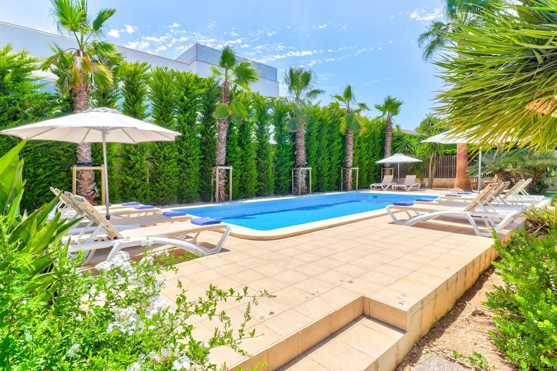 An outdoor swimming pool sits beside a tiled deck with lounge seating and umbrellas.