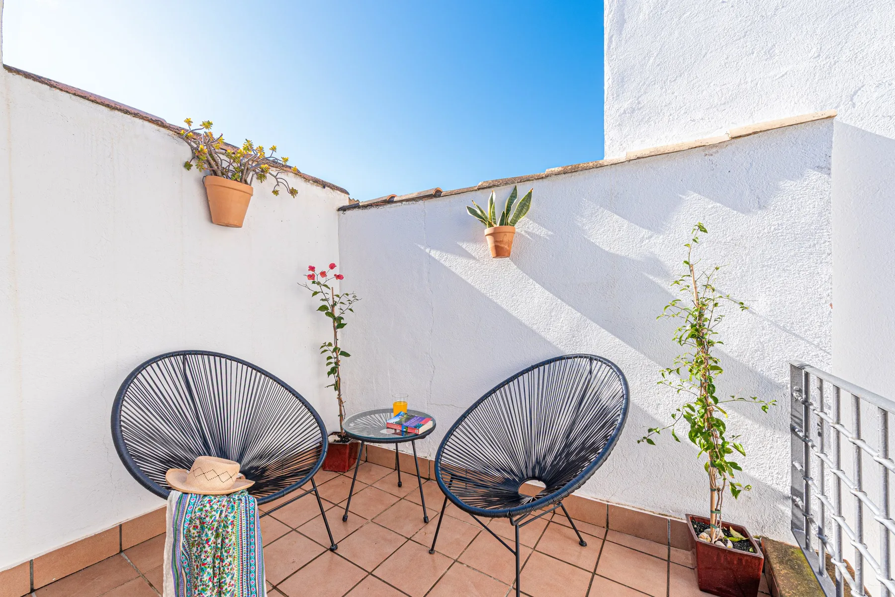 Un pequeño patio exterior con dos asientos tejidos y plantas en macetas.