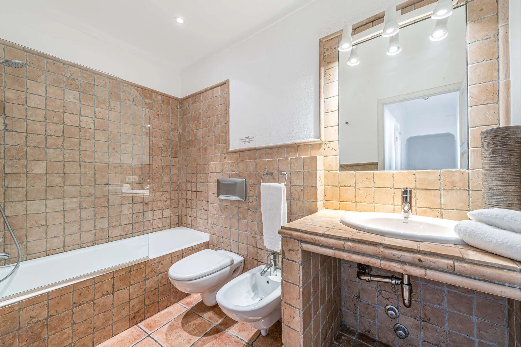 Baño con azulejos, bañera, inodoro, bidé y lavabo bajo un espejo grande.