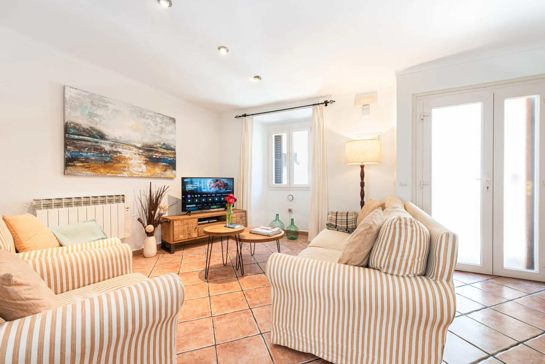 Una sala luminosa con asientos a rayas, un televisor y una puerta de vidrio.