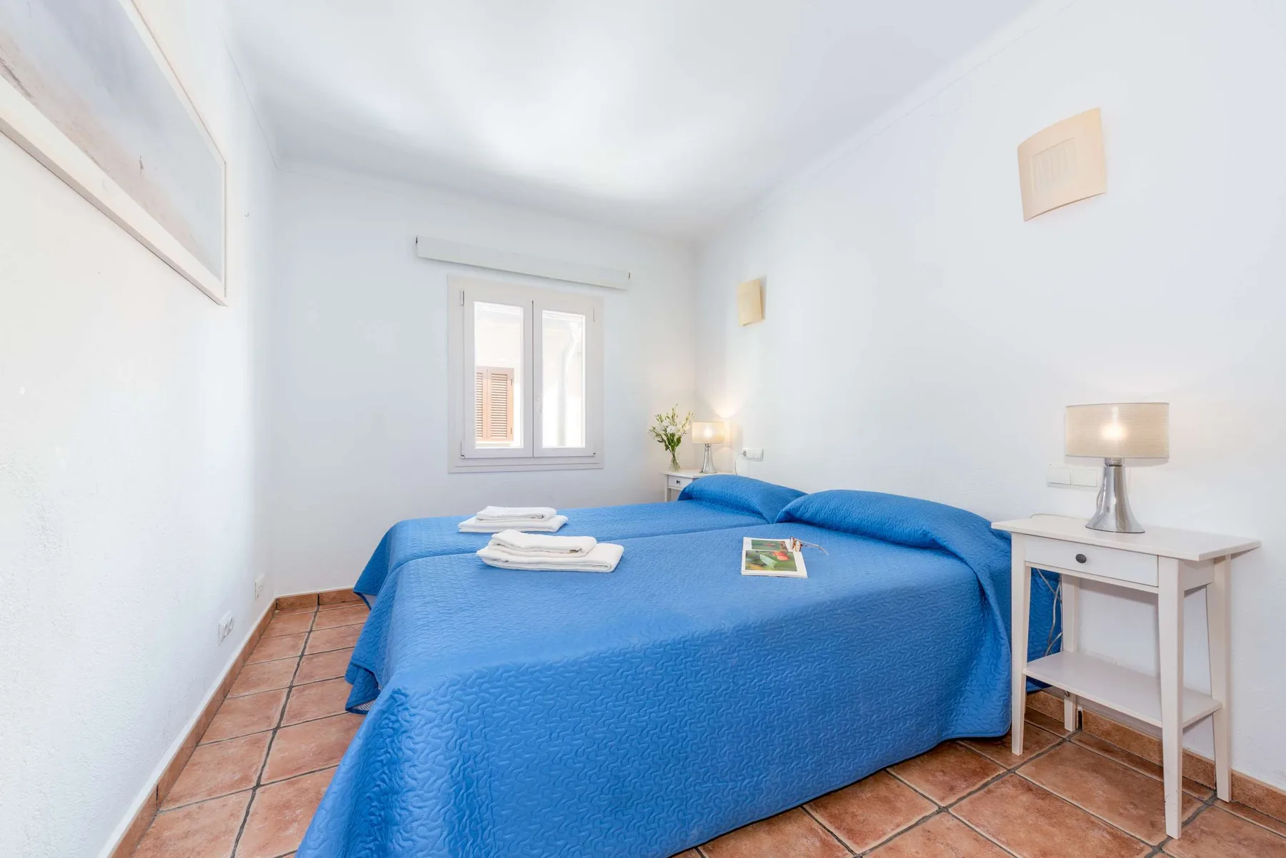 Dormitorio con camas cubiertas de azul y una ventana en la pared del fondo.