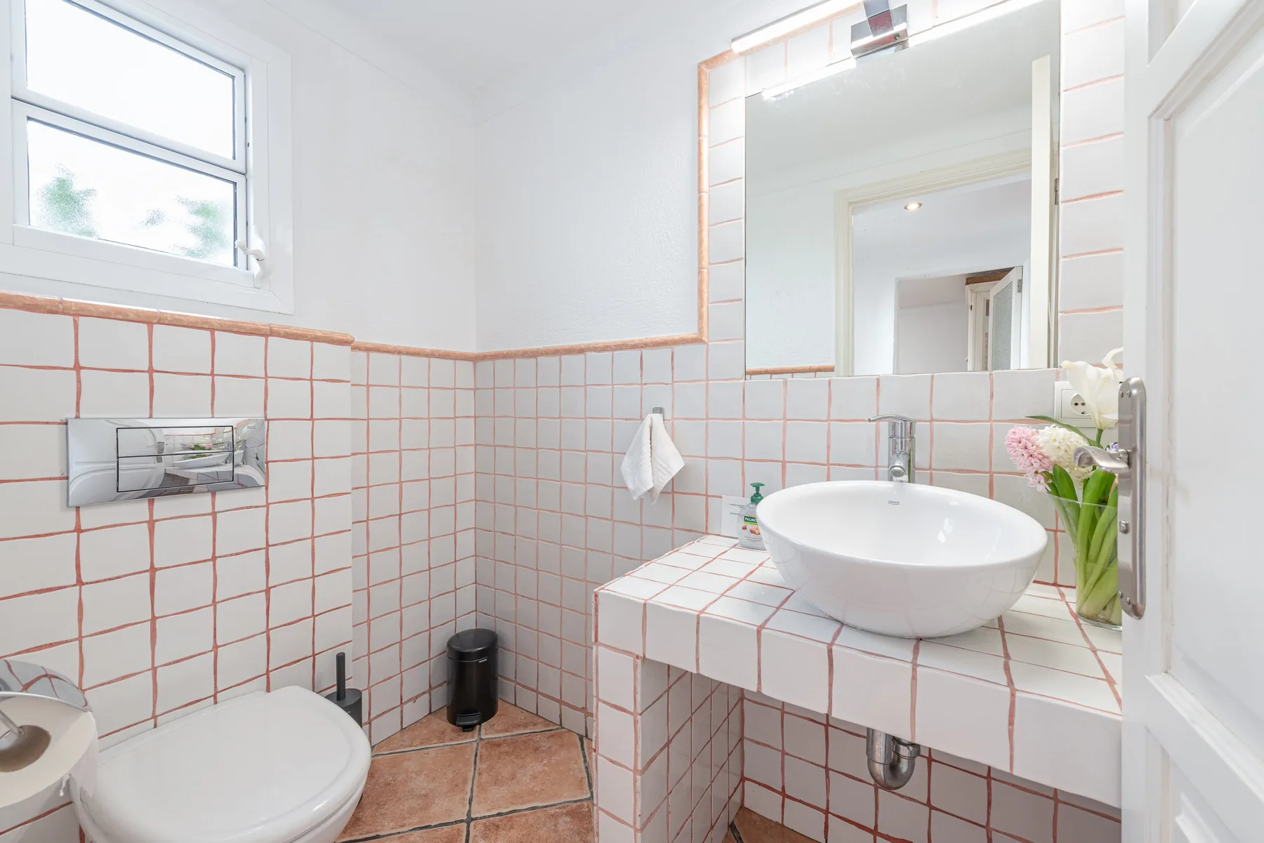 Un baño luminoso con azulejos, lavabo, inodoro y un espejo grande.