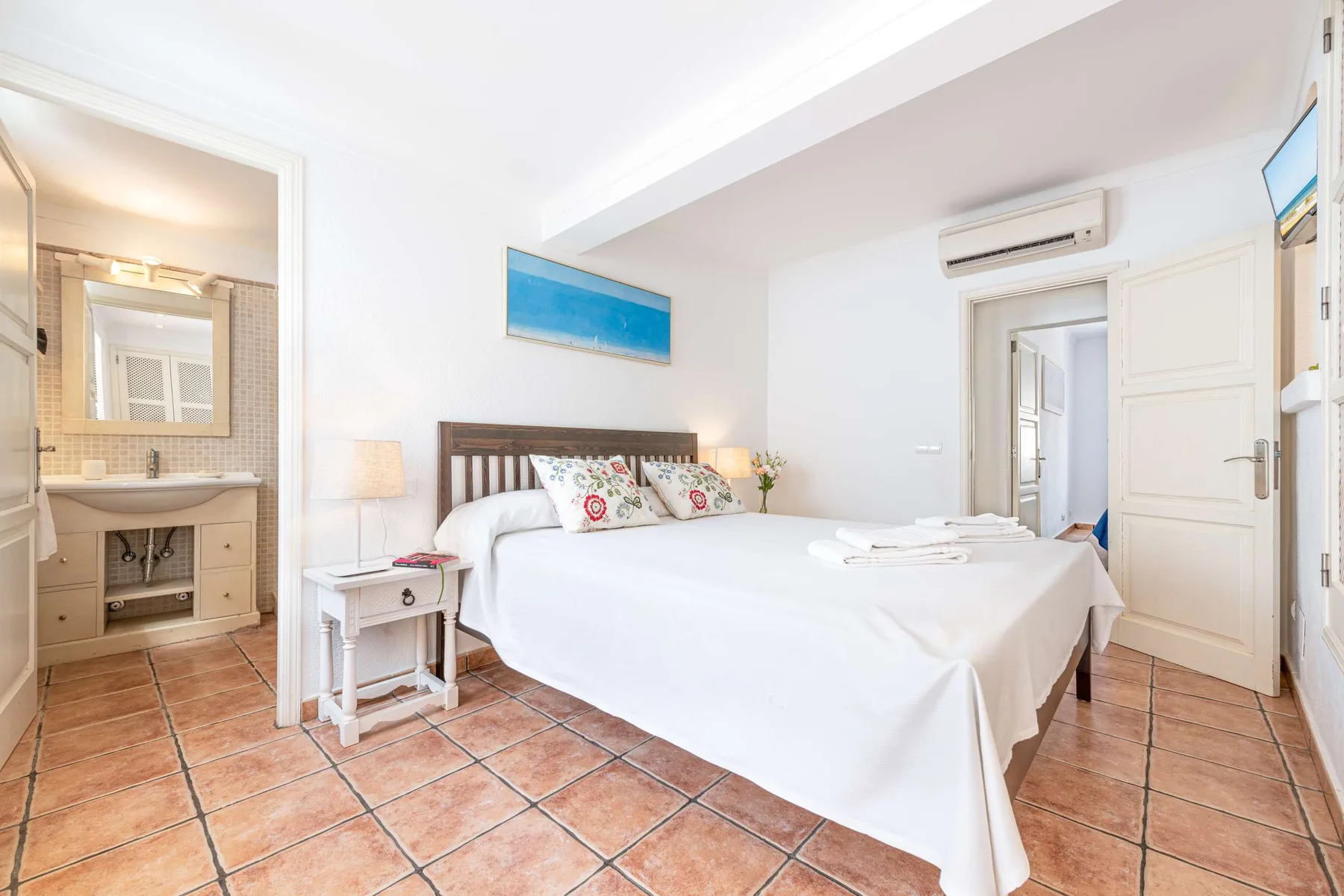 Un dormitorio luminoso con una cama doble, una mesita y suelo de baldosas.