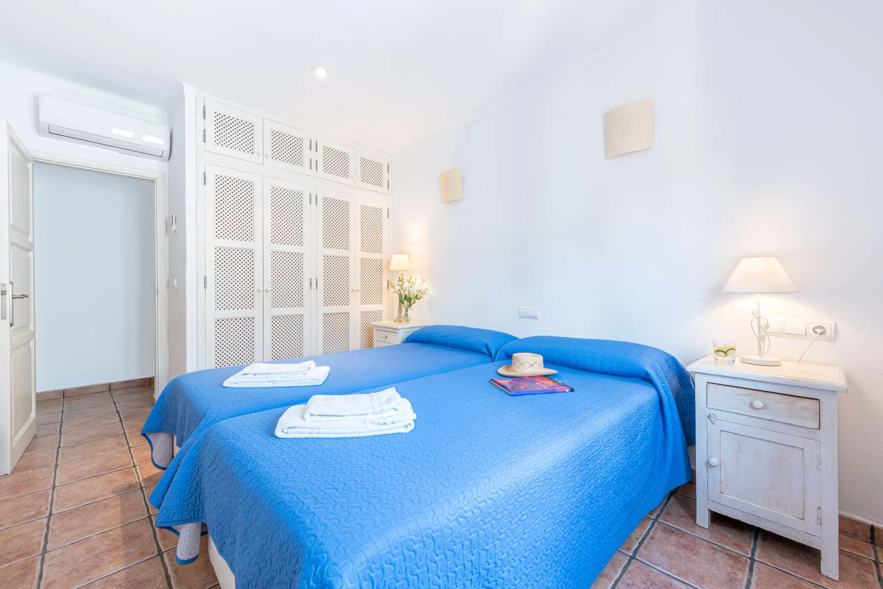 Un dormitorio luminoso con ropa de cama azul y mesillas blancas.