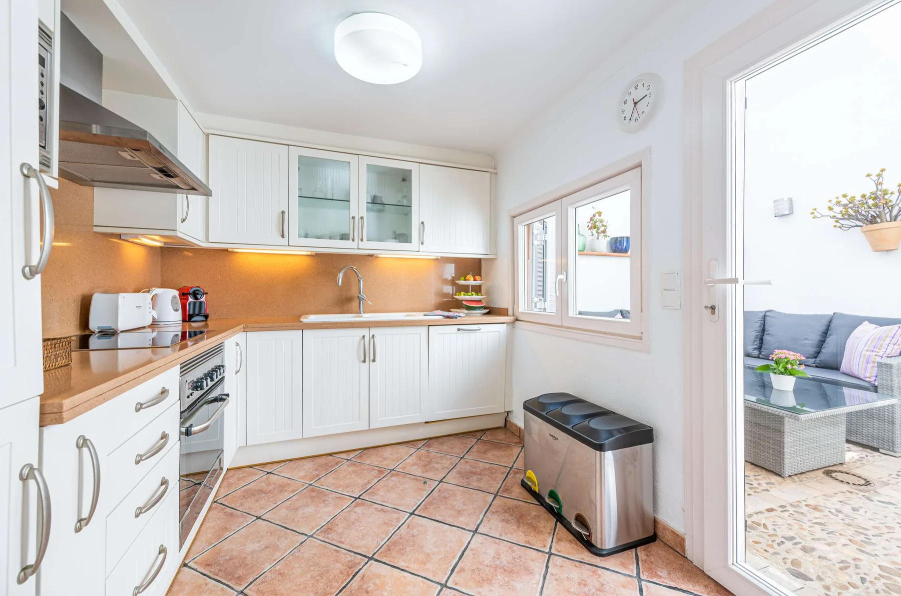 Una cocina luminosa con armarios blancos, suelo de baldosas y una ventana pequeña.