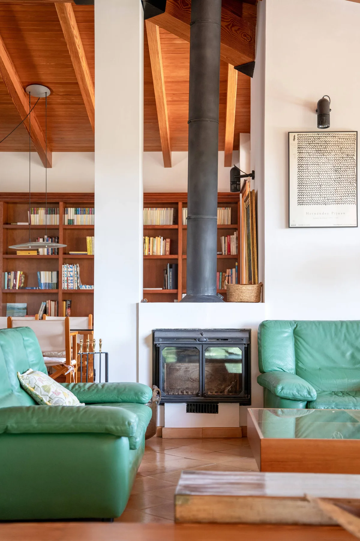 Una sala de estar con asientos verdes, estanterías y una estufa de leña.
