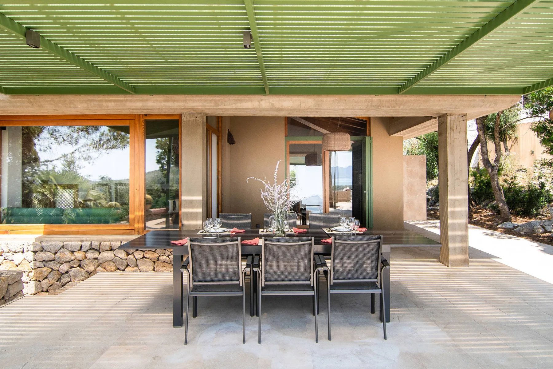 Una zona de comedor exterior cubierta con una mesa y sillas junto a grandes ventanales.