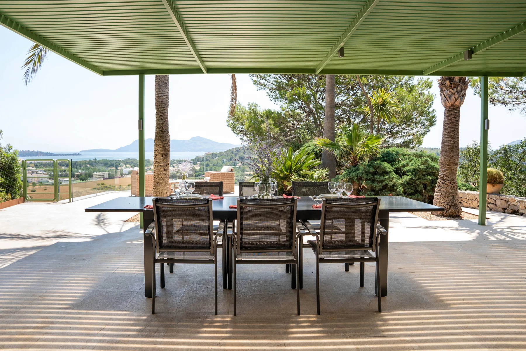 Una zona de comedor exterior cubierta con mesa y sillas da a un paisaje verde.