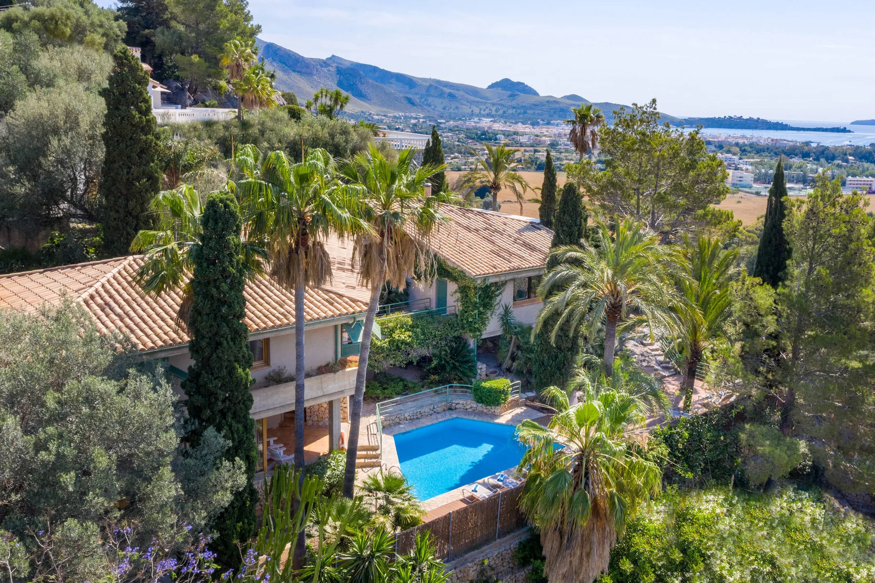 Una casa y una piscina están rodeadas de árboles, con montañas a lo lejos.