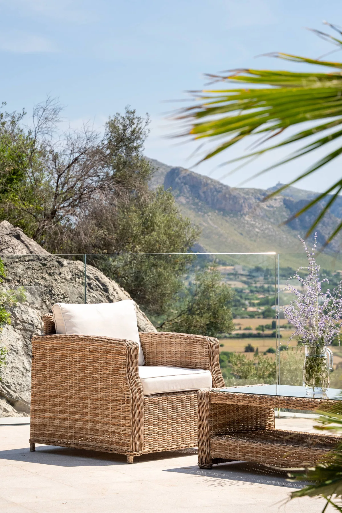 Asientos al aire libre junto a una barandilla de vidrio con vistas a un valle verde.