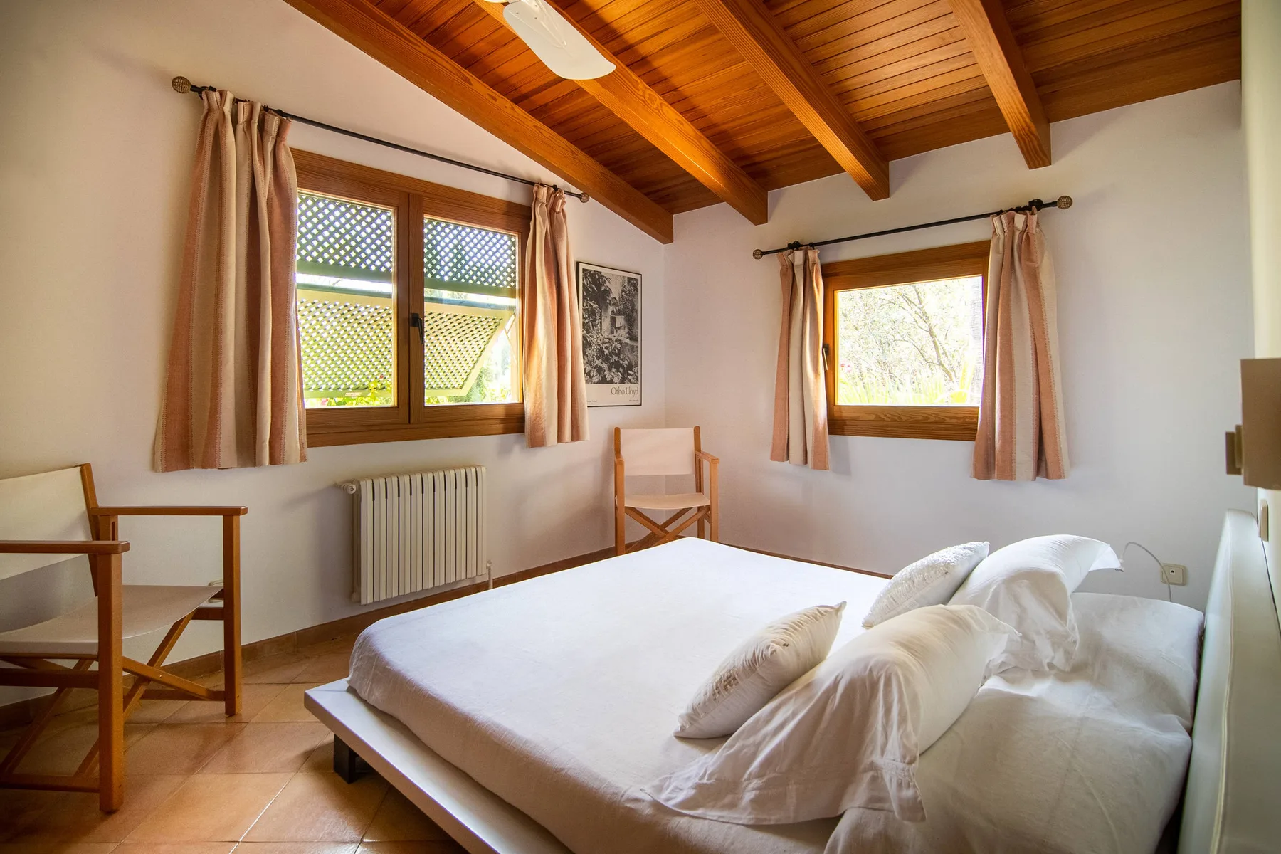 Un dormitorio con una cama, vigas de madera en el techo y ventanas con cortinas.