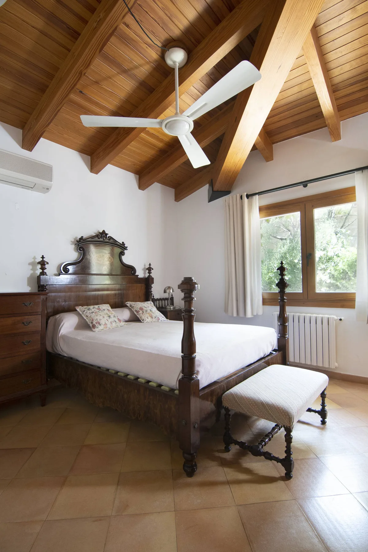 Un dormitorio con una cama de madera bajo un alto techo de vigas y una ventana.