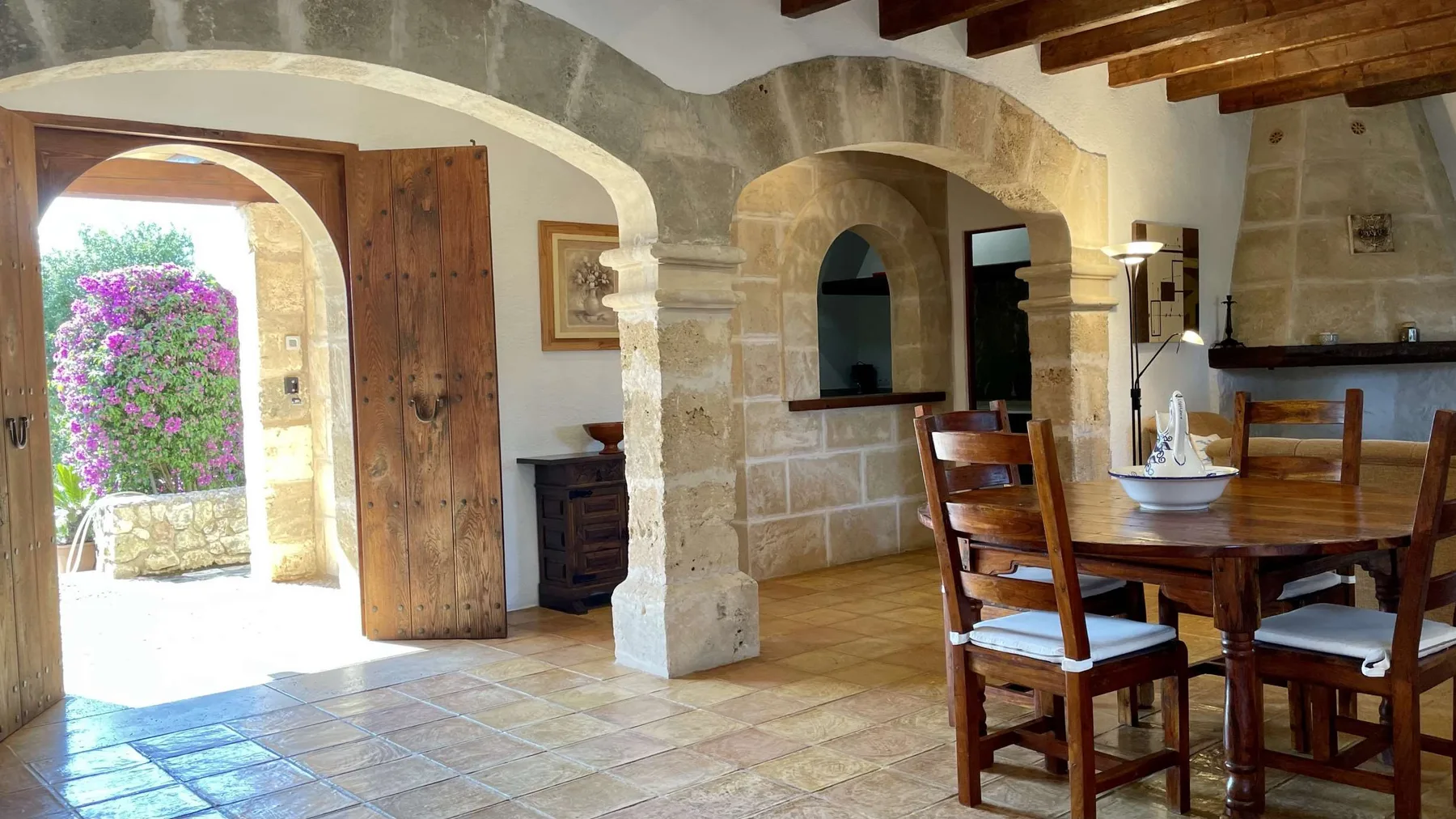 Comedor de piedra con una mesa y sillas de madera junto a una entrada arqueada.