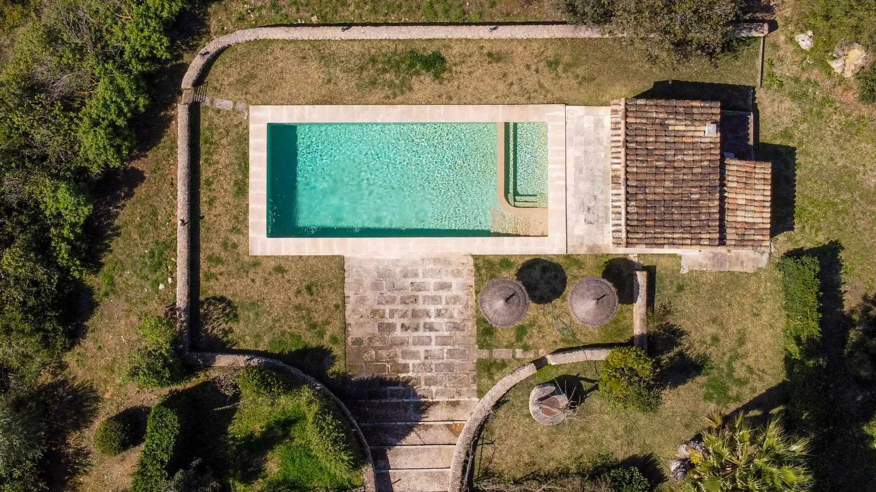 Vista aérea de una piscina exterior junto a un patio pavimentado y un jardín.