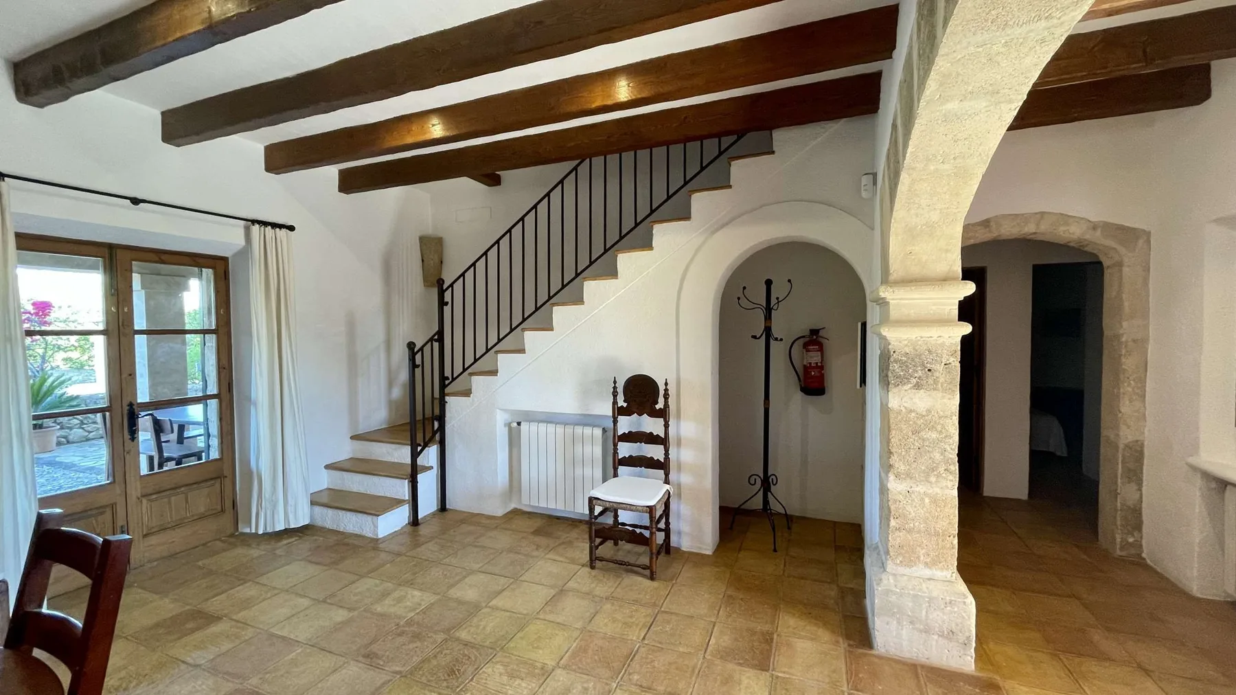 Interior con suelo de piedra, una escalera, vigas de madera en el techo y una puerta acristalada.