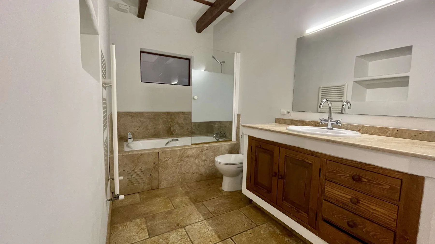 Un baño con bañera, inodoro y un mueble de lavabo largo.