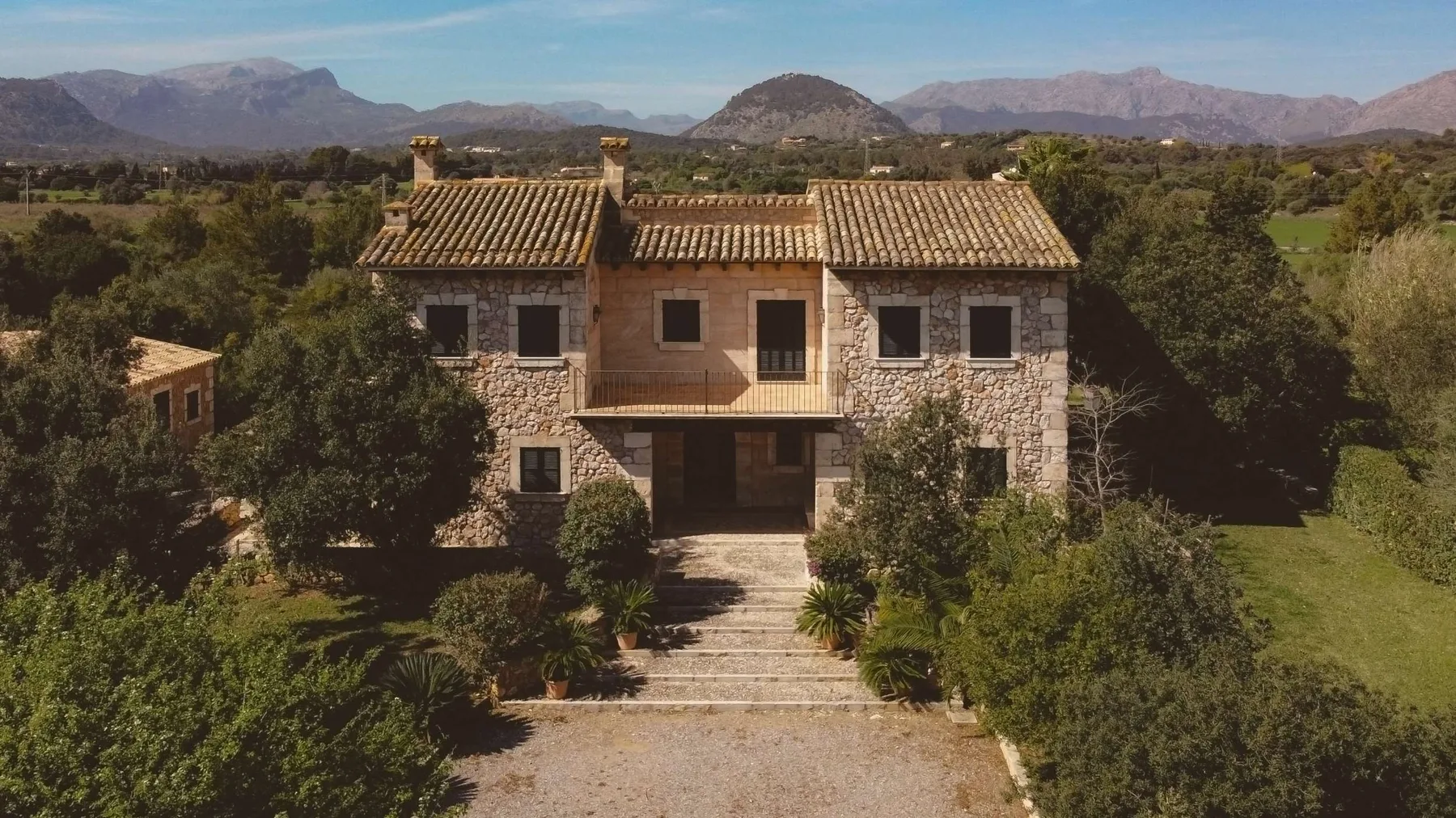 Una casa de piedra está rodeada de árboles, con montañas al fondo.