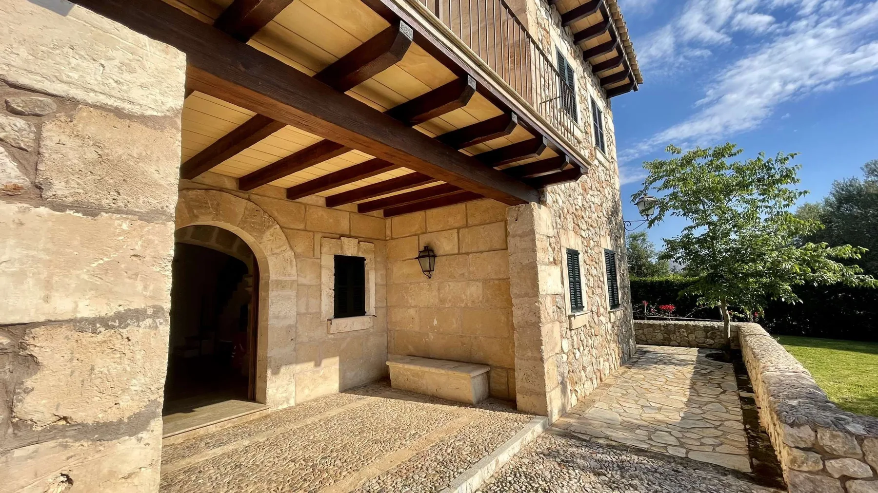 La entrada de un edificio de piedra da a una terraza pavimentada bajo un balcón de madera.