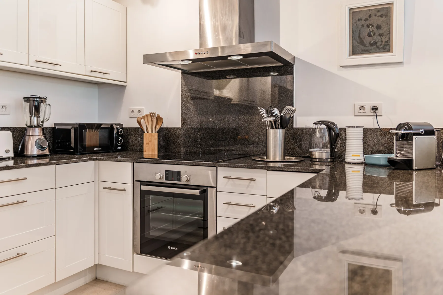 Una cocina moderna con gabinetes blancos, encimeras oscuras y electrodomésticos de acero inoxidable.