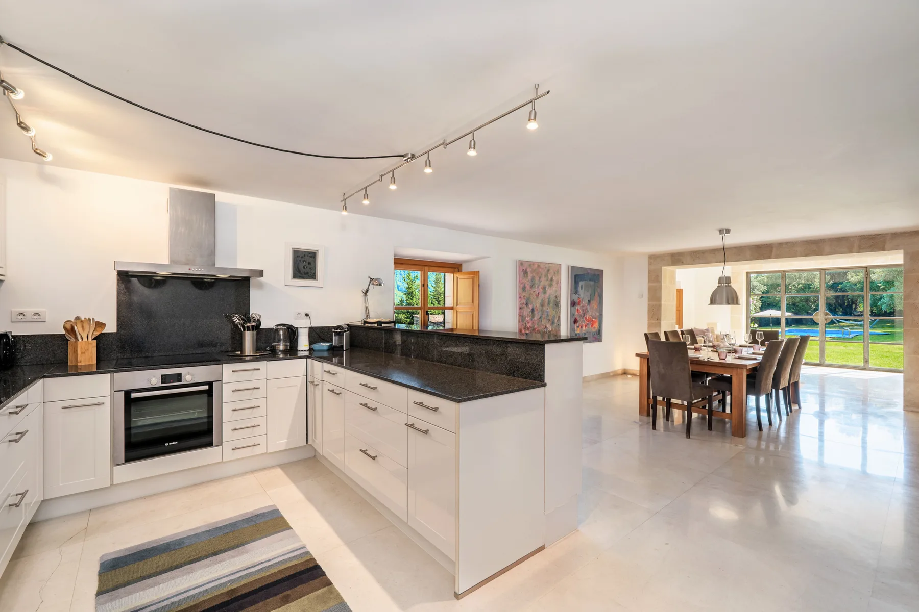 Una cocina abierta al comedor, con muebles blancos y una mesa grande.