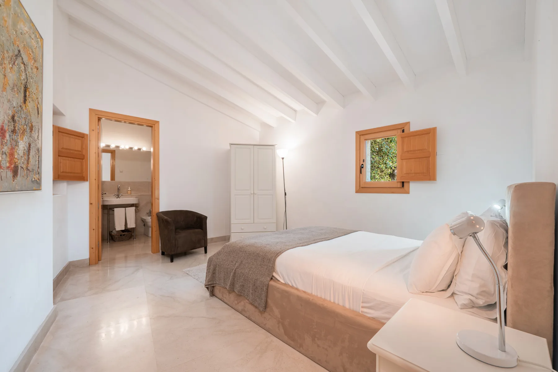 Dormitorio luminoso con una cama, una ventana pequeña y una puerta abierta hacia el baño.