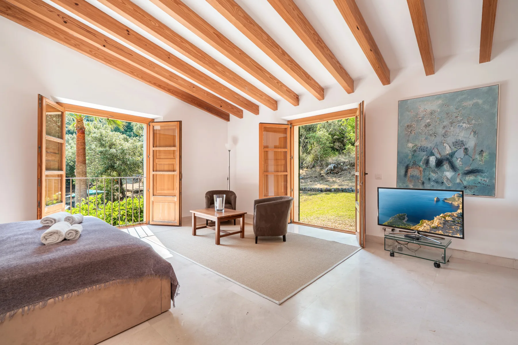 Un dormitorio luminoso con puertas abiertas, vigas expuestas y una zona de estar.