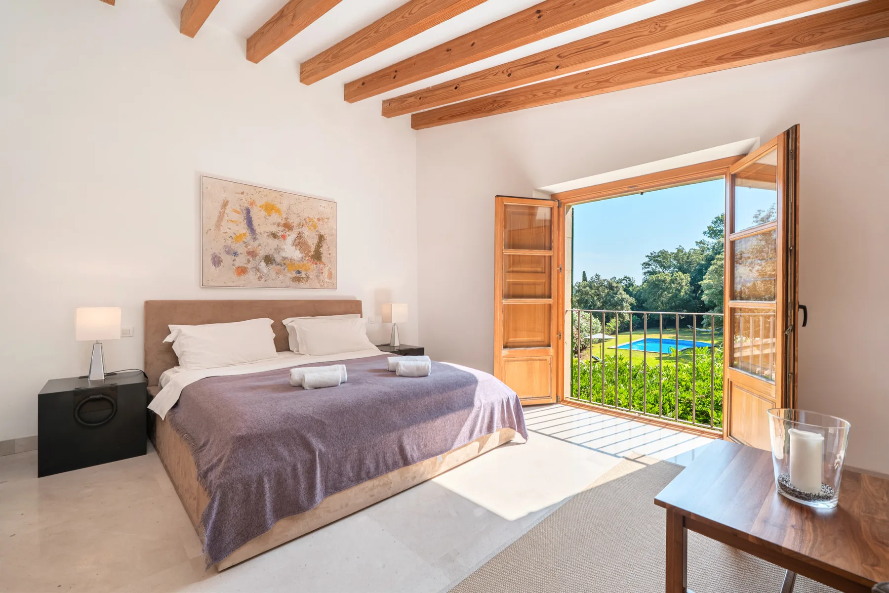 Un dormitorio con una cama junto a puertas de madera abiertas que dan a una zona verde exterior.