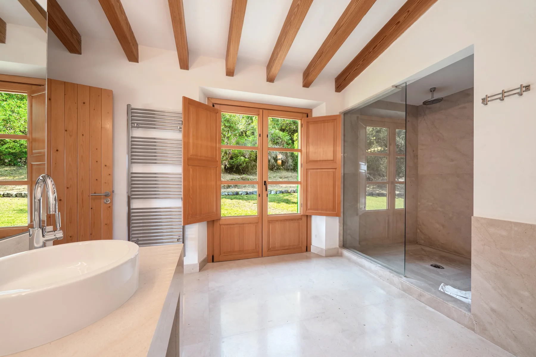 Un baño luminoso con bañera, ducha de cristal y grandes ventanas.