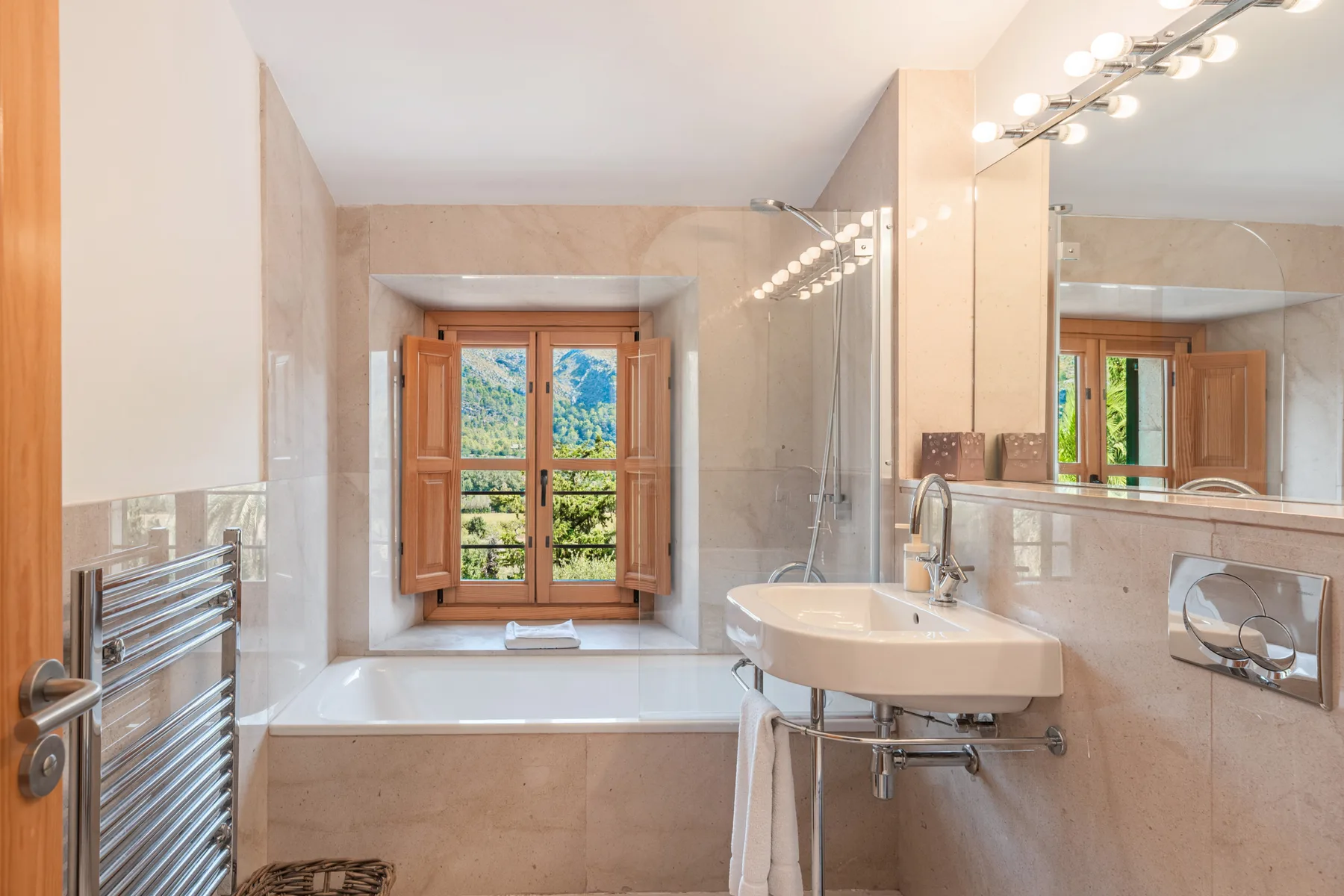 Un baño luminoso con bañera bajo una ventana de marco de madera y un lavabo.