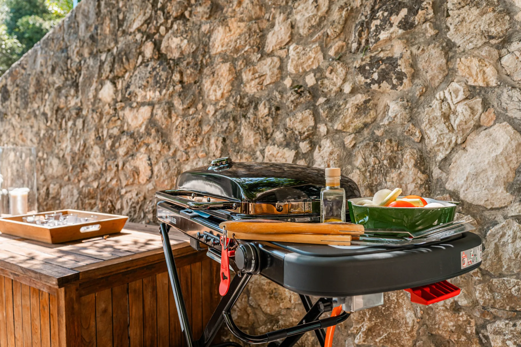 Una parrilla al aire libre y platos para servir están junto a un muro de piedra.