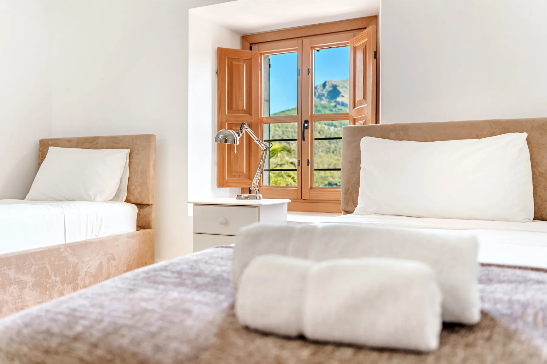 Un dormitorio luminoso con camas junto a una ventana de marco de madera.