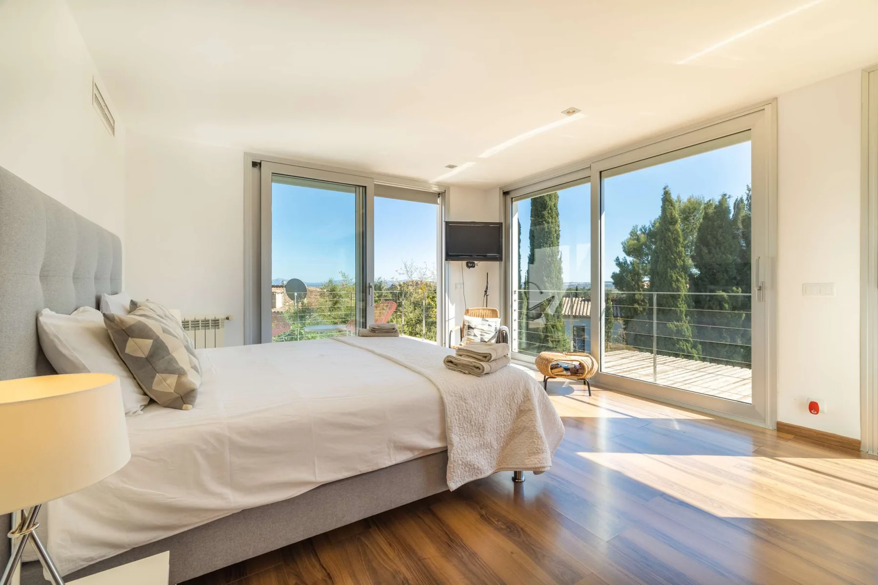 A bright bedroom with a bed beside large glass doors opening onto a balcony.