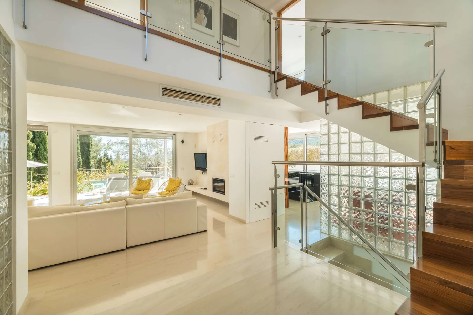A bright living room with seating beside large windows and a staircase.