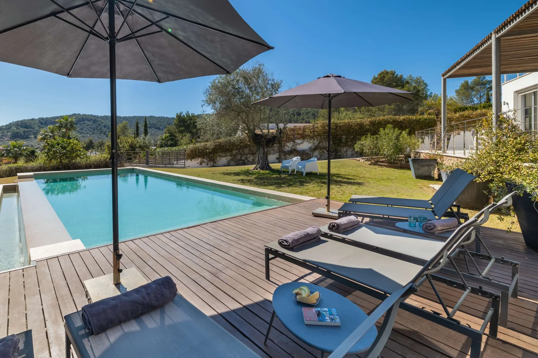 An outdoor pool beside a wooden deck with lounge seating and umbrellas.