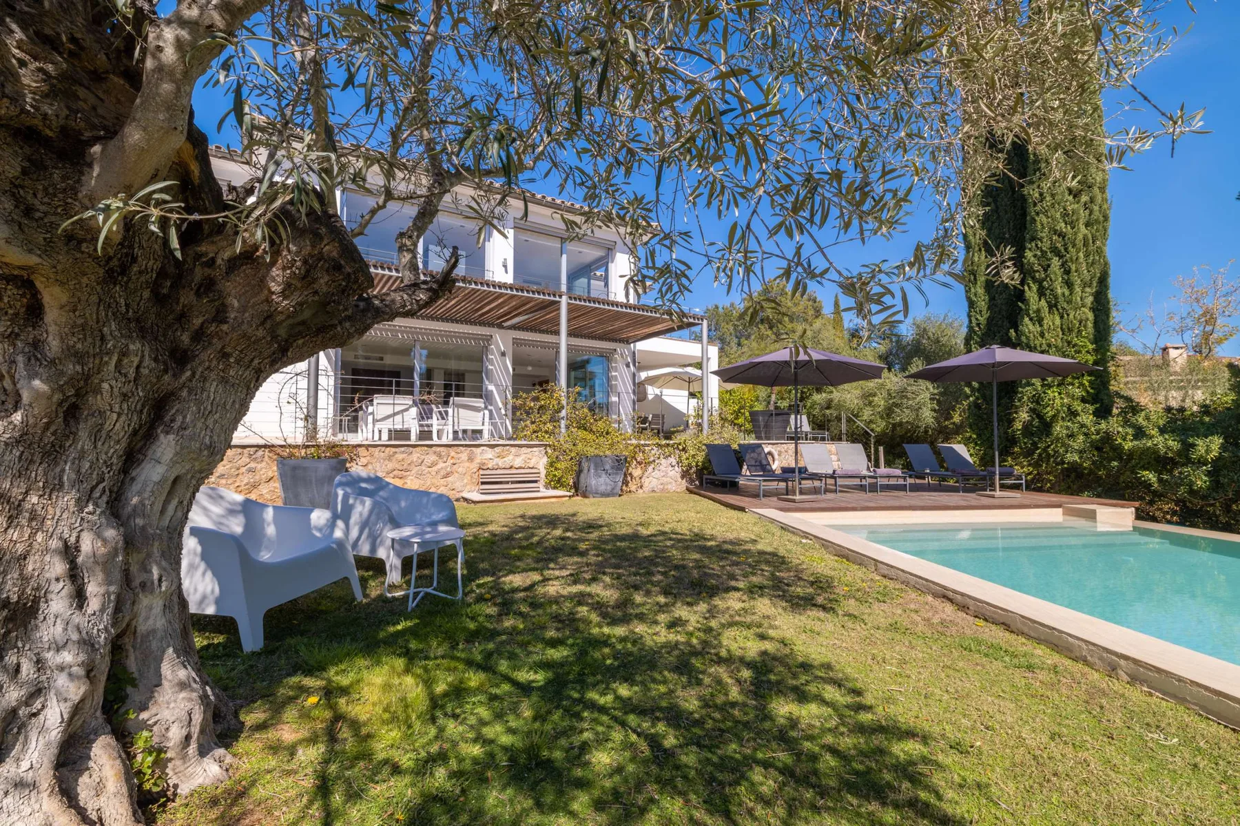 Outdoor scene with a house, lawn, and swimming pool beneath a clear blue sky.