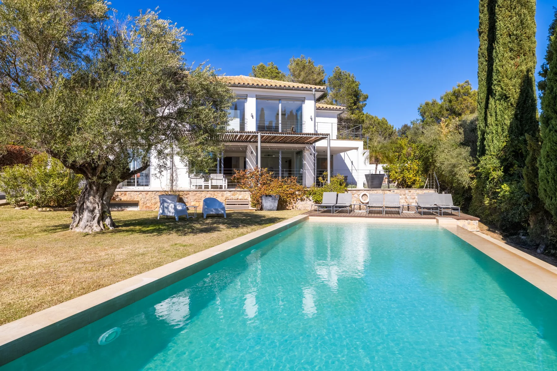 A swimming pool in front of a two-story house, surrounded by trees.