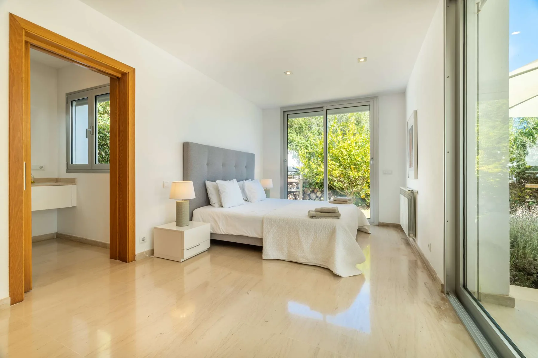 A bright bedroom with a bed beside large glass doors.