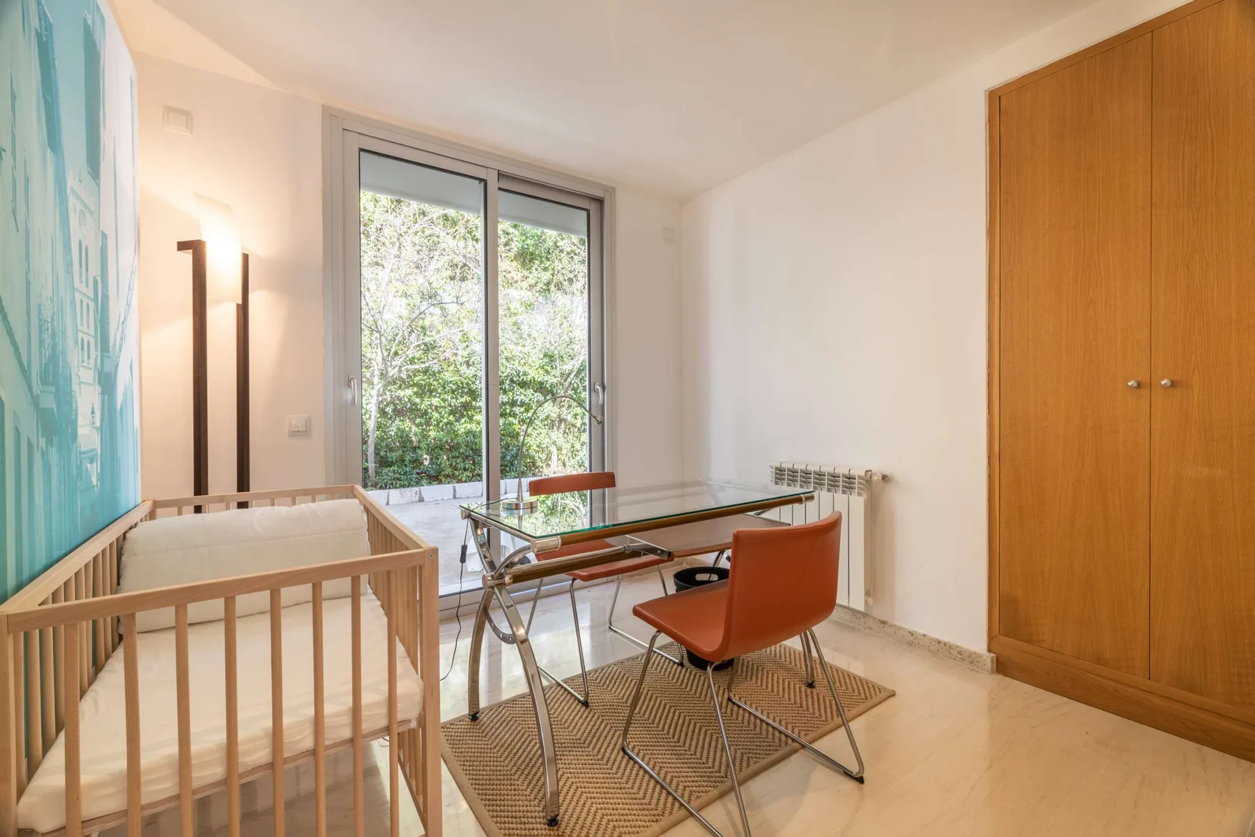 A bright room with a desk, seating, a large window, and a wooden wardrobe.
