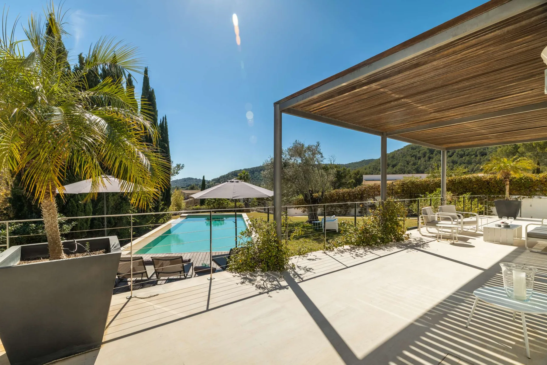 A sunny outdoor terrace overlooks a swimming pool, with shaded seating nearby.